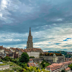Fototapeta premium Historic Bern Cityscape with Cathedral Spire Under Dramatic Cloudy Sky
