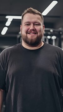 A young, overweight man poses smiling inside a gym.