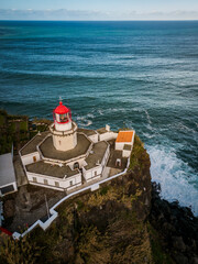 Aerial vertical view of Arnel Lighthouse (Farol do Arnel) with steep winding road on a cliff at sunset, Sao Miguel, Azores.