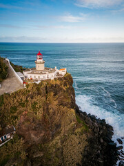 Aerial vertical view of Arnel Lighthouse (Farol do Arnel) with steep winding road on a cliff at sunset, Sao Miguel, Azores.