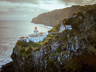 Aerial vertical view of Arnel Lighthouse (Farol do Arnel) with steep winding road on a cliff at sunset, Sao Miguel, Azores.