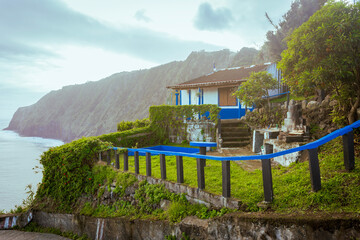 Aerial vertical view of Arnel Lighthouse (Farol do Arnel) with steep winding road on a cliff at sunset, Sao Miguel, Azores.