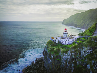 Aerial vertical view of Arnel Lighthouse (Farol do Arnel) with steep winding road on a cliff at sunset, Sao Miguel, Azores.