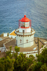 Aerial vertical view of Arnel Lighthouse (Farol do Arnel) with steep winding road on a cliff at sunset, Sao Miguel, Azores.