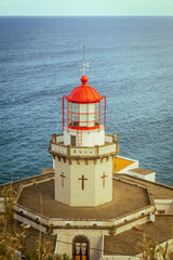 Aerial vertical view of Arnel Lighthouse (Farol do Arnel) with steep winding road on a cliff at sunset, Sao Miguel, Azores.