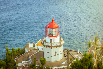 Aerial vertical view of Arnel Lighthouse (Farol do Arnel) with steep winding road on a cliff at sunset, Sao Miguel, Azores.