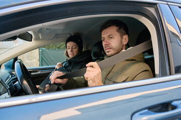 Man fastening seat belt in driver seat while woman sits in passenger seat inside car