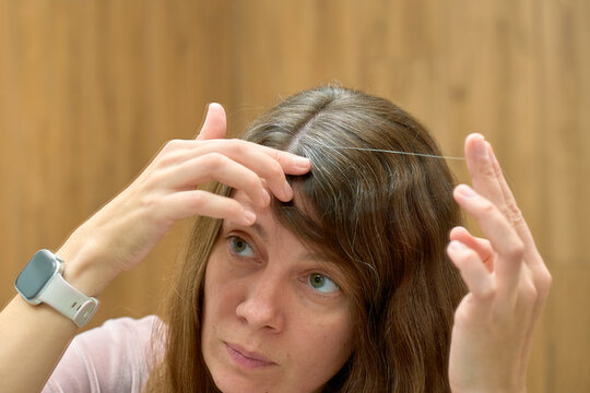 Woman examining hair roots and gray strands while looking at mirror
