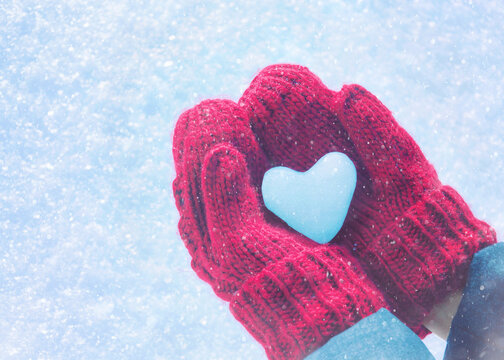 Hands in knitted mittens with heart of snow in winter day. Love concept. Valentine day background.	