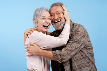 Fototapeta premium Portrait of positive, smiling senior couple, handsome man hugging beautiful woman on blue background