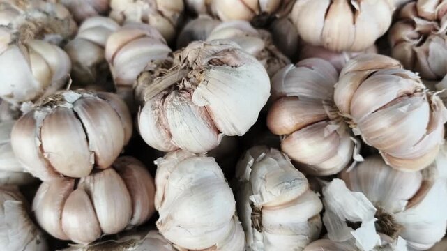 Cinematic slow-motion zoom out revealing a vast pile of raw white garlic with dry skins at a local Indonesian bazaar, showcasing organic agricultural produce.