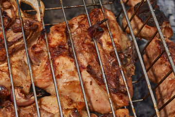 Juicy pieces of chicken are grilled in a metal grill over hot coals. The ruddy crust and smoky aroma emphasize the atmosphere of a picnic and a summer vacation in nature.