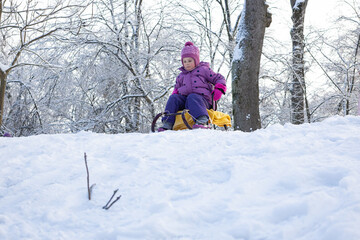 Child on sled descending gentle snowy hill at family park