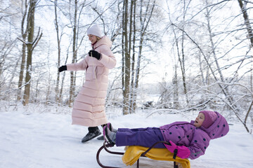 Young woman in pink down jacket walking on snowy path in winter forest park
