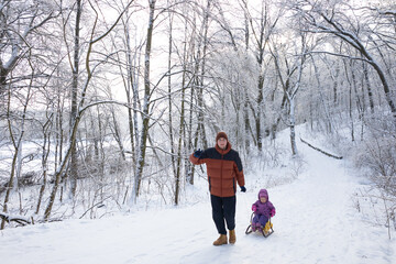 Father and little daughter enjoying winter day together with sled in snowy forest