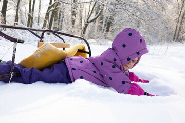 Little girl in warm winter suit crawling and playing in deep snow on a sunny day