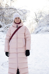 Beautiful young woman in warm winter clothes posing in snowy forest on sunny day