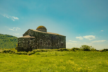 Historic stone church standing in a green meadow under a clear blue sky. Representing cultural heritage, rural architecture, peaceful countryside scenery and timeless religious history. Turkey.