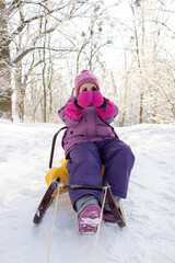 Playful little girl in winter gear hiding her face with pink gloves in snowy forest