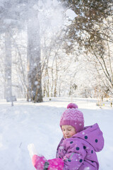 Happy child enjoying snowfall and playing with snow in magical sunny winter forest park