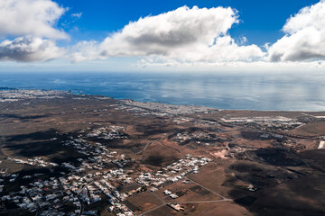 Aerial view shows Lanzarote volcanic plain to the Atlantic, Arrecife and port on the coast, villages and plots on lava terrain, and the airport with long runways. © Aerial Film Studio
