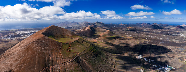 Aerial view of Lanzarote shows La Geria lava rock vineyards, Timanfaya peaks, whitewashed villages, and the Atlantic under cumulus clouds in clear daytime light. © Aerial Film Studio