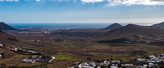 Aerial view of Lanzarote volcanic interior toward the Atlantic, La Geria lava fields and vineyards, Arrecife on the coast, cone shaped hills, fincas, and palm lined villages. © Aerial Film Studio
