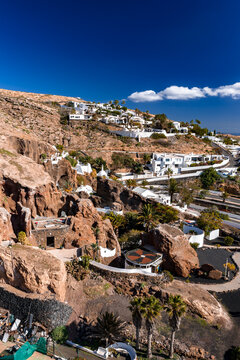 Sunlit whitewashed villas step down volcanic cliffs at Lagomar Casa Museo in Lanzarote, Canary Islands. Terraced roads curve, domes and cave doorways add contrast.