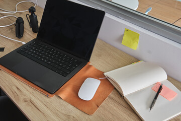 Workspace with a laptop, mouse, notebook, and pen on a wooden desk, reflecting productivity