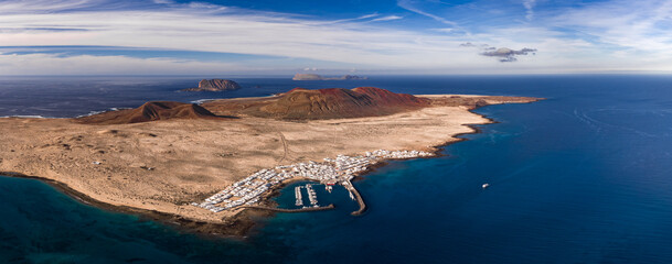 Aerial view of La Graciosa with Caleta de Sebo, arid lava plains, rust cinder cones, Montana Clara and Alegranza on horizon, and Mirador del Rio across the strait. © Aerial Film Studio