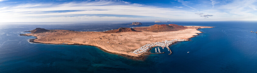 Aerial view of La Graciosa near Lanzarote, Canary Islands, with ochre cones, Caleta de Sebo marina, turquoise shore, and Montana Clara and Alegranza in clear daylight. © Aerial Film Studio