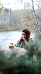 Naklejka premium A sweet woman with curly hair drinks tea and relaxes on the terrace of her house on an autumn day. Health care, sincerity, a sense of balance and calm.