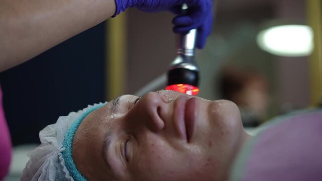 Cosmetologist performing a non-surgical facelift on a female client's skin. The patient is getting a radiofrequency facial treatment