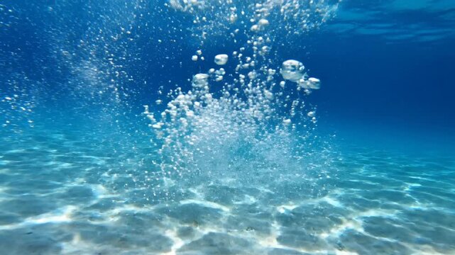 Person diving into clear blue ocean water, creating bubbles, underwater scene with sunlight