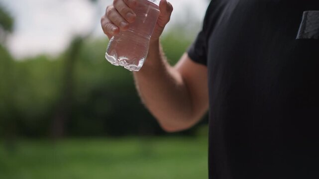 Man Opening Water Bottle Outdoors, Man Twists Cap On Water Bottle Outside, Outdoor Athlete Uncaps Water For Hydration Pause, Muscular Man With Tattoos Prepares To Hydrate After Exercise Outside