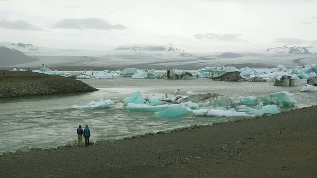 Two people stand along a river in the frozen Arctic, Jokulsarlon, glacier lagoon in Iceland, suggesting global warming.