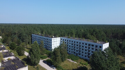 Fototapeta premium Aerial view of an abandoned residential building surrounded by forest in the Baltic region. Urban decay, forgotten architecture and nature reclaiming human structures.