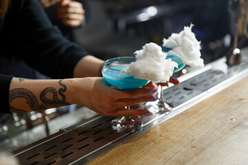 Bright blue cocktails topped with cotton candy are served at a trendy bar during the evening hours