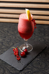 Refreshing red berry drink with lemon garnish served in a glass on a dark textured background
