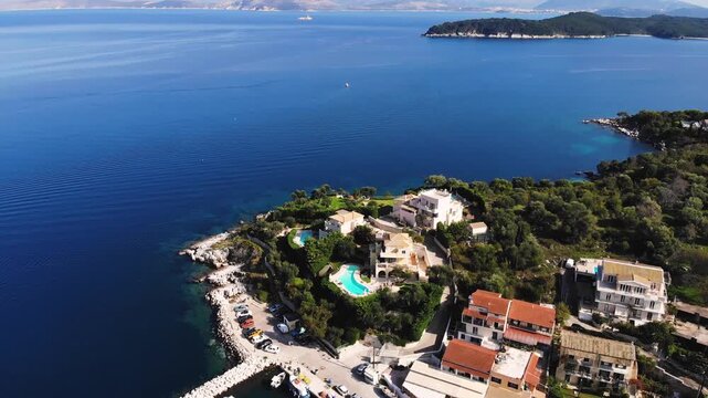 Aerial drone view of Kassiopi, coast sea village in northeast coast of Corfu island, Ionian Islands, Kerkyra, Greece in a summer sunny day, with marina, town, beach and castle, Greek landscape