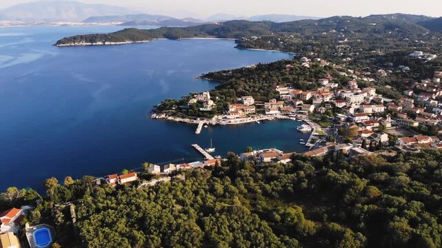 Aerial drone view of Kassiopi, coast sea village in northeast coast of Corfu island, Ionian Islands, Kerkyra, Greece in a summer sunny day, with marina, town, beach and castle, Greek landscape