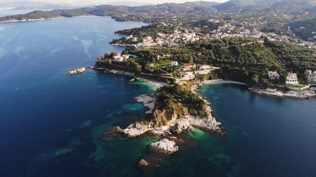 Aerial drone view of Kassiopi, coast sea village in northeast coast of Corfu island, Ionian Islands, Kerkyra, Greece in a summer sunny day, with marina, town, beach and castle, Greek landscape