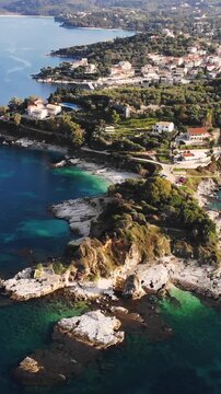 Aerial drone view of Kassiopi, coast sea village in northeast coast of Corfu island, Ionian Islands, Kerkyra, Greece in a summer sunny day, with marina, town, beach and castle, Greek landscape