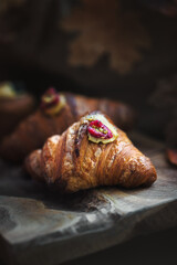 Fresh gourmet croissant topped with raspberry and pistachios on a rustic wooden board in moody dark lighting.