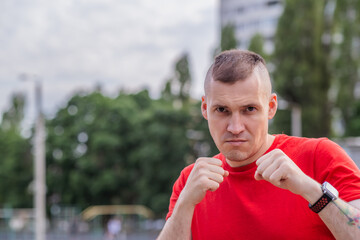 A man demonstrates a fighting stance with a fierce expression, ready to spar. He stands in a park,...