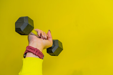 A hand holding a dumbbell against a bright yellow wall in a fitness setting, highlighting strength...