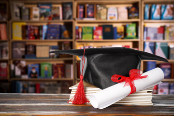 Diploma, graduate cap and notebooks on wooden table in library. Scroll with red ribbon
