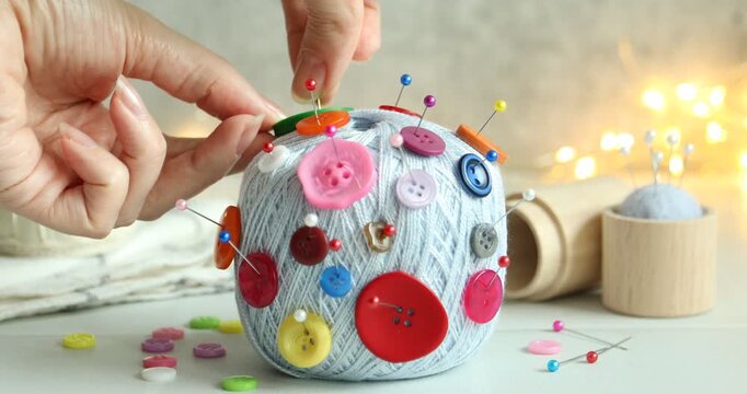 Woman sticking pin and button into skein of yarn at white table, closeup