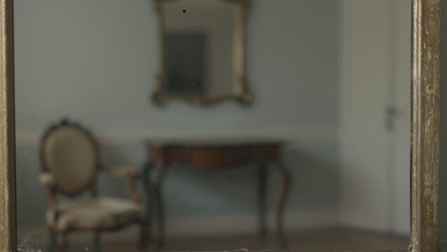 Antique gold framed mirror reflecting a console table and chair in a room