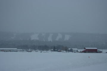 Fototapeta premium A snowy view of a farm with a mountain ski park in the background during winter